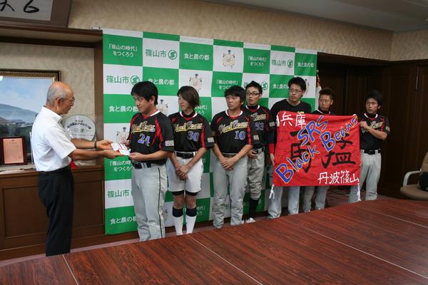 奨励金を市長から手渡されている代表者とその様子を見ているチームの写真